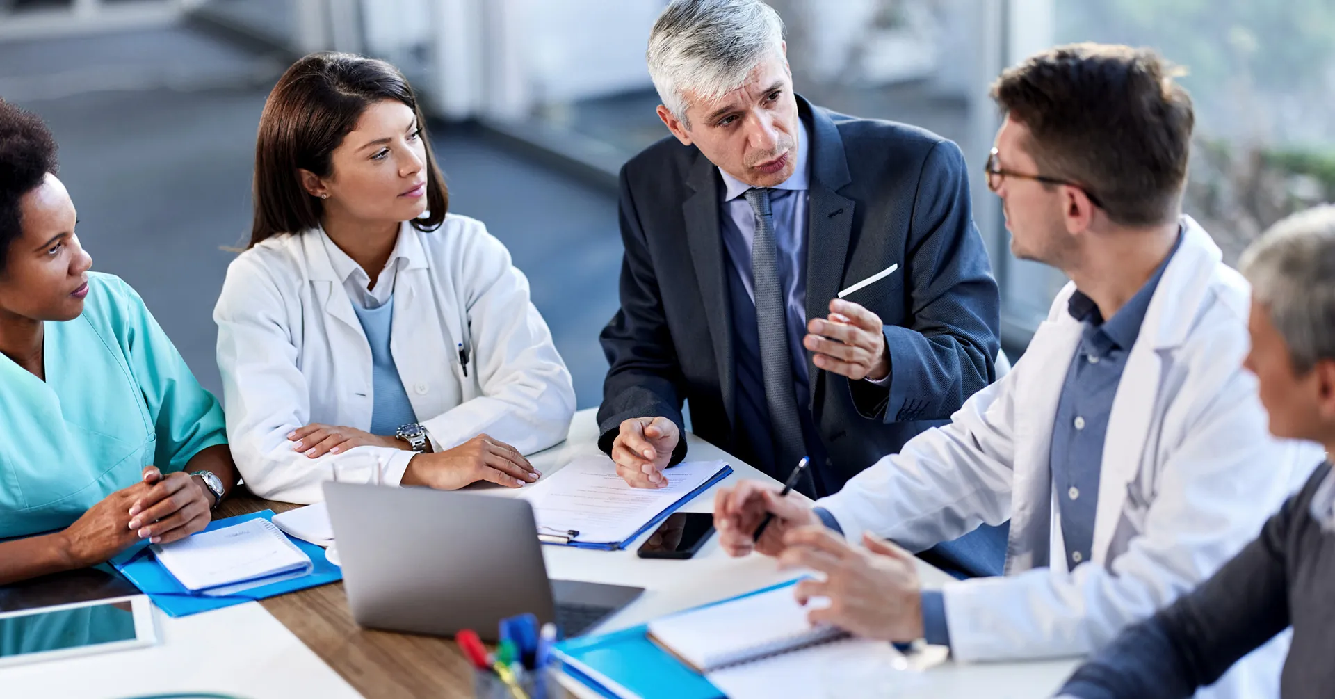 Team of healthcare leaders sit at a conference table discussing emergency plans.