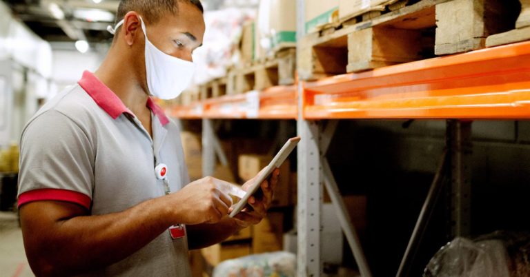 warehouse employee in mask looking at tablet device