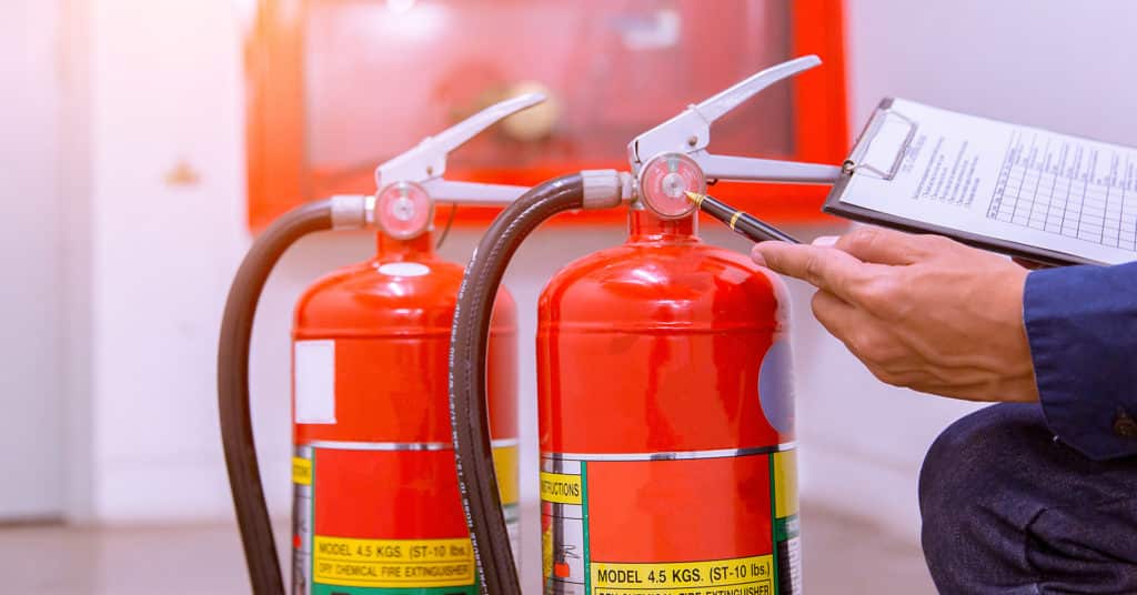 Employee referring to fire safety checklist by fire extinguishers
