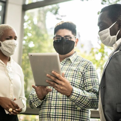 three people in masks looking at an electronic tablet