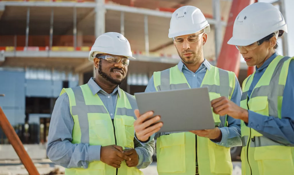 three people in safety gear and hard hats reviewing project plans