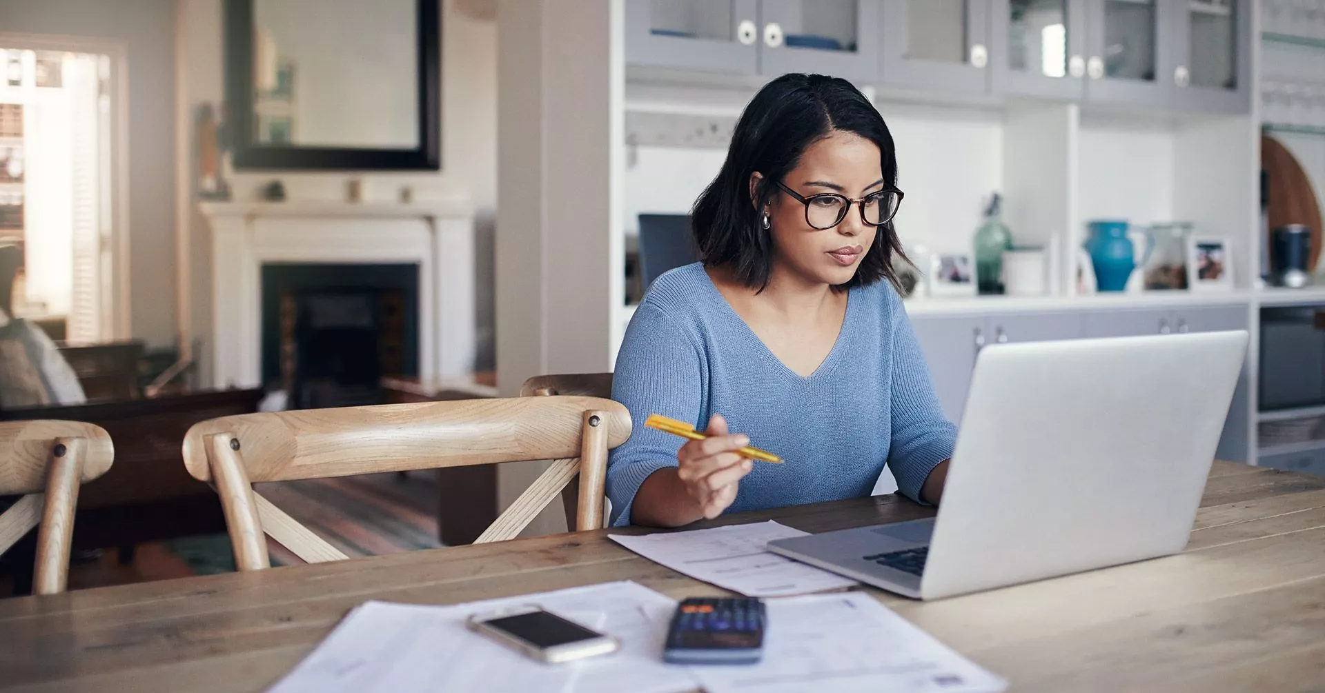 woman at table with laptop and papers scattered on desk