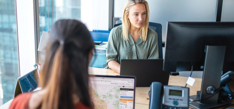 two women sitting adjacent desks looking at threat monitoring information on a computer