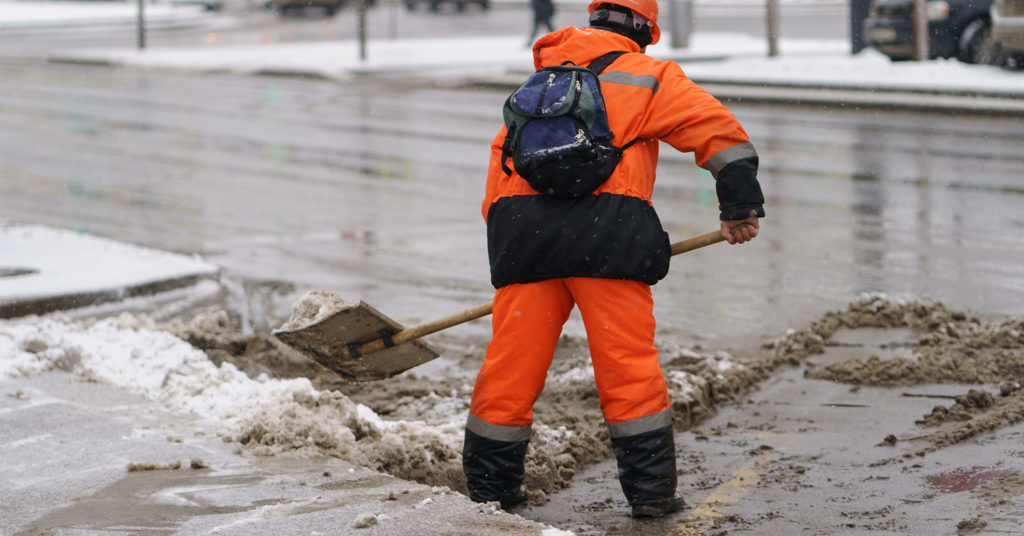 person shoveling snow in cold-weather working gear