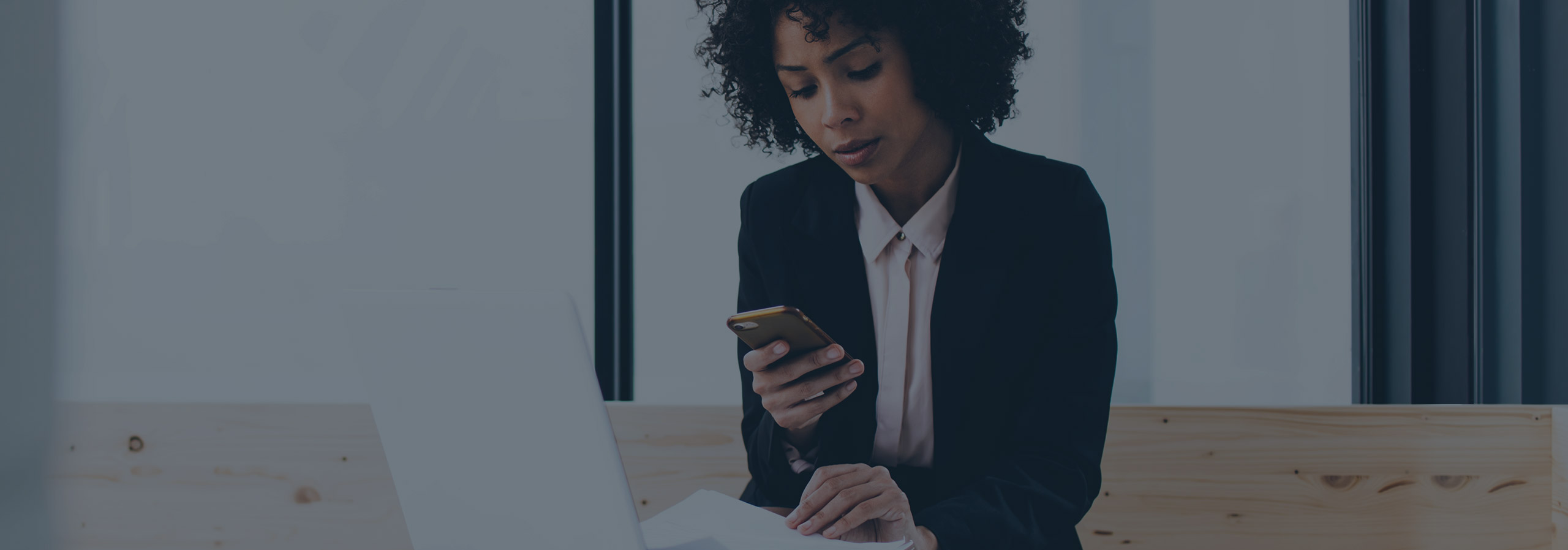 woman in black blazer and pink blouse looking at a smartphone