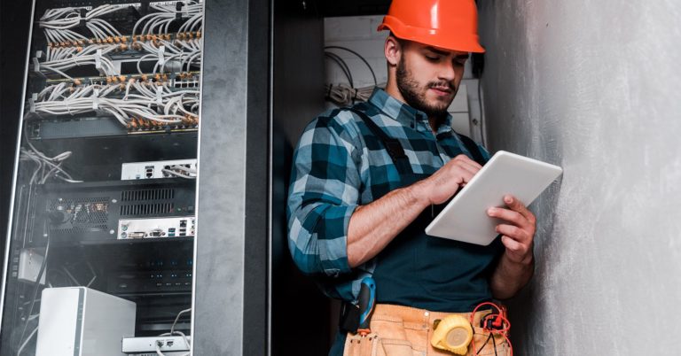 Field worker holding tablet in front of networking equipment