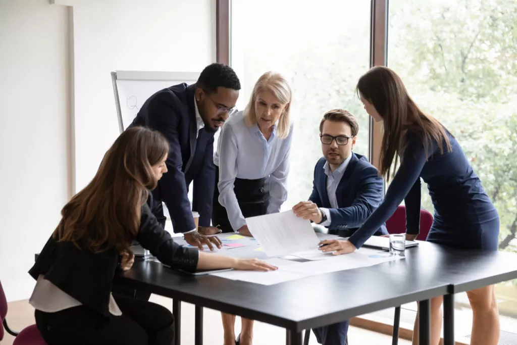 Five employees reviewing plans in a meeting