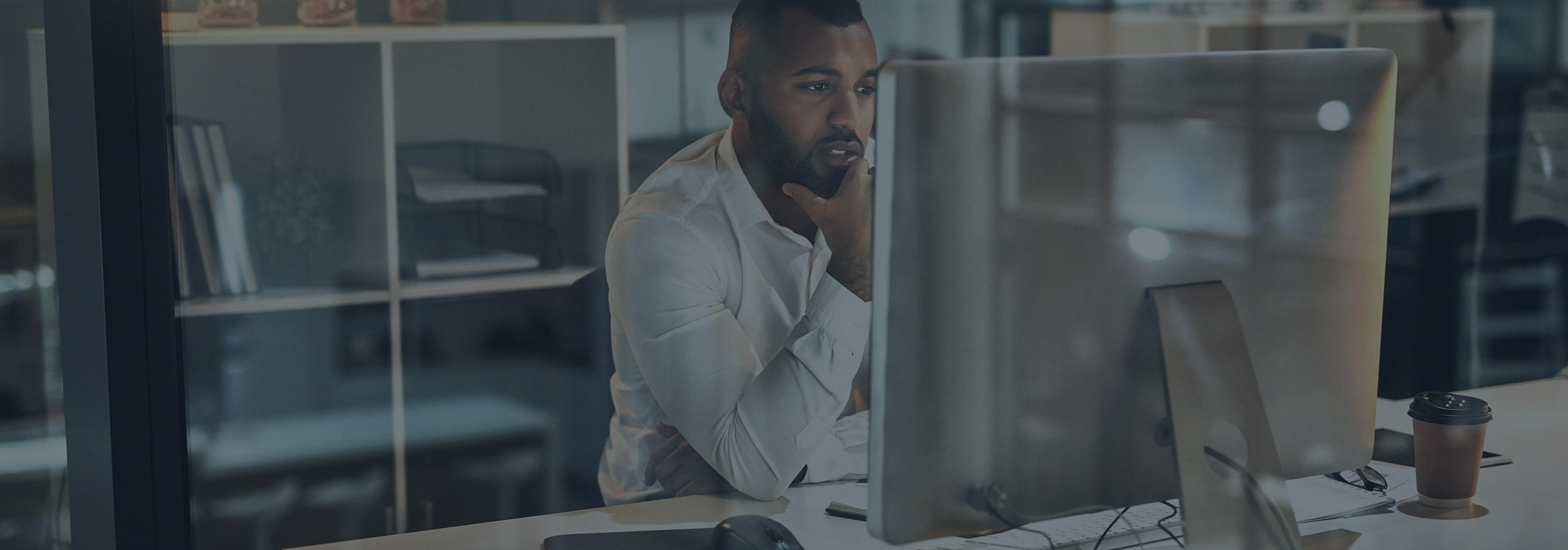 man in white collared shirt sitting behind desktop computer with hand on chin