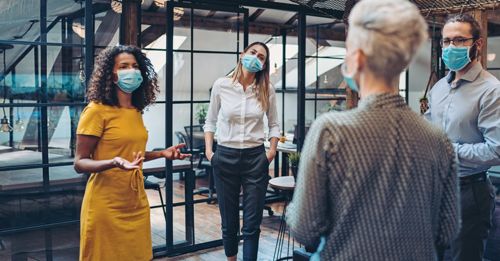 four colleagues, all wearing protective masks, discuss their return to work strategy