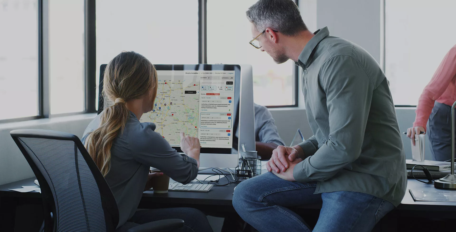 a man observes a woman sits at a computer and composes a notification in the AlertMedia platform