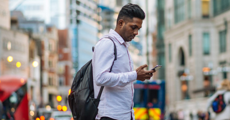 Man with backpack crossing street while checking emergency alert on phone