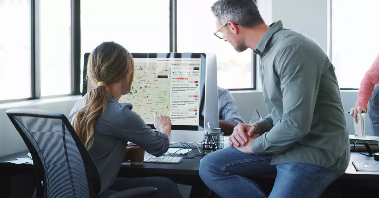 two colleagues looking at desktop computer monitor with AlertMedia threat software map showing