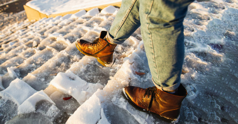 Someone going down a set of snow-covered stairs that pose a risk to slips trips and falls