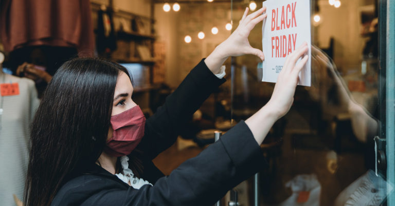 Retail employee wearing mask hanging sign for Black Friday sale