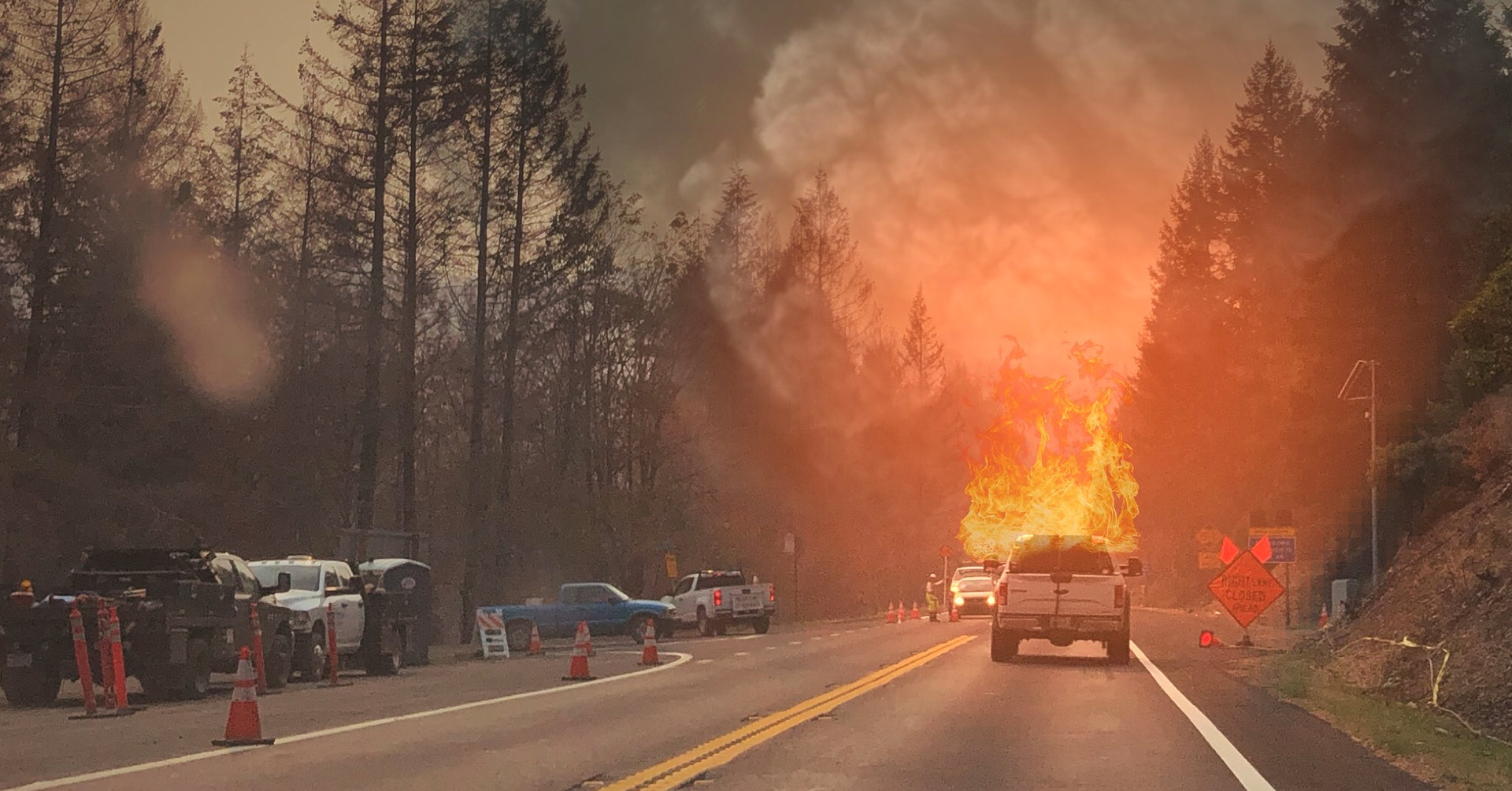 wildfire on road surrounded by trees and a road crew