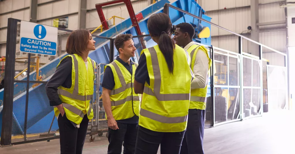 Workers wearing hi-vis vests huddle in a meeting