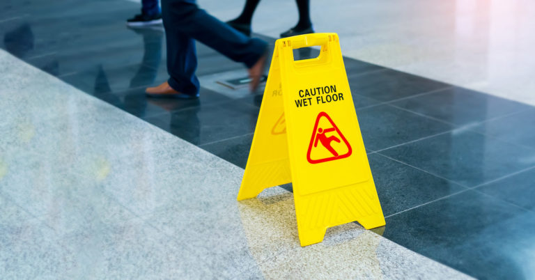 A "caution wet floor sign" in an entryway to prevent slips trips and falls with people walking past.