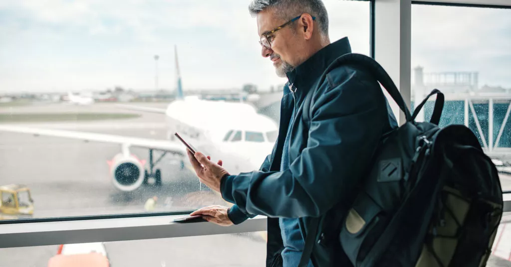 A business travel checks his phone for weather alerts.