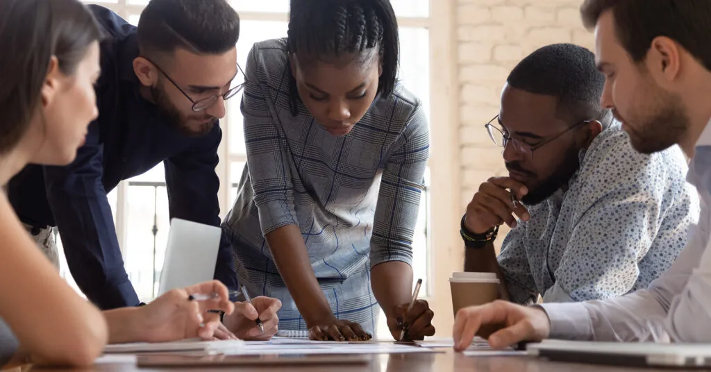 Five people gather around a conference table, discussing a plan and taking notes