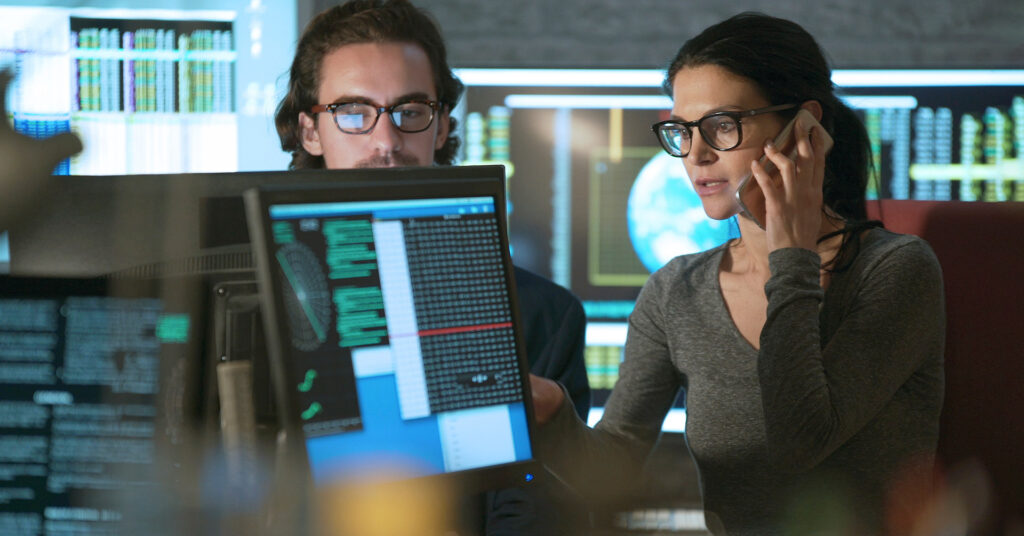 Workers discuss cybersecurity at a desktop computer