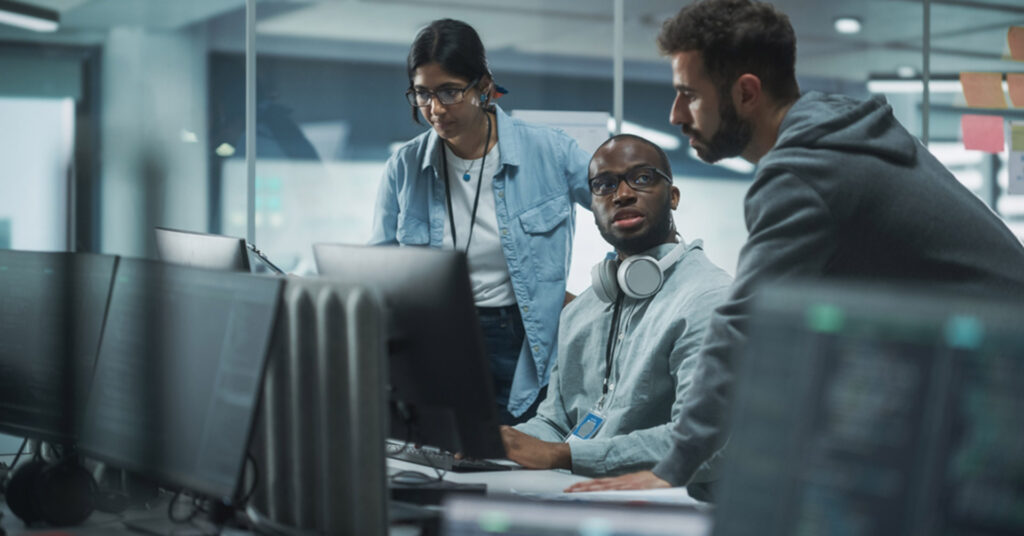 Workers stand over desktop computer