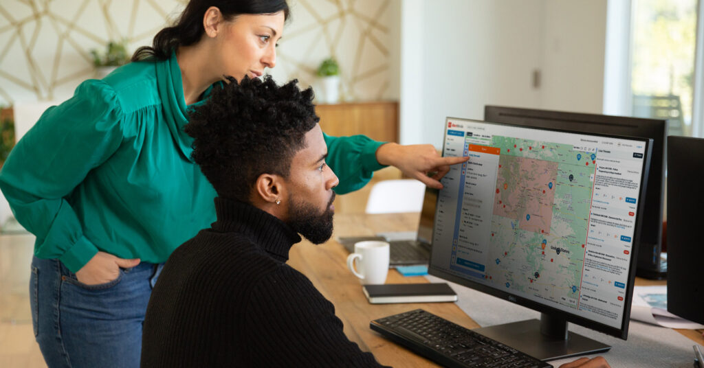 Two safety leaders review a map of travel risks on the computer.