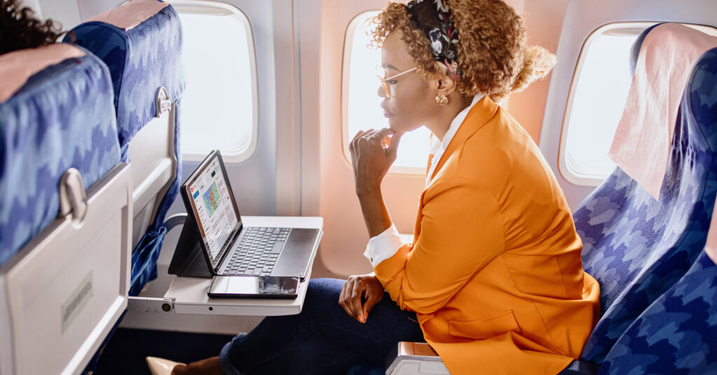 A woman travels on a plane, looking at her laptop and AlertMedia's Travel Risk Management solution.