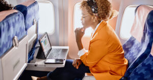 A woman travels on a plane, looking at her laptop and AlertMedia's Travel Risk Management solution.