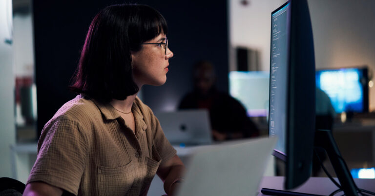 A woman looks intently at a computer screen, monitoring security threats and operations.