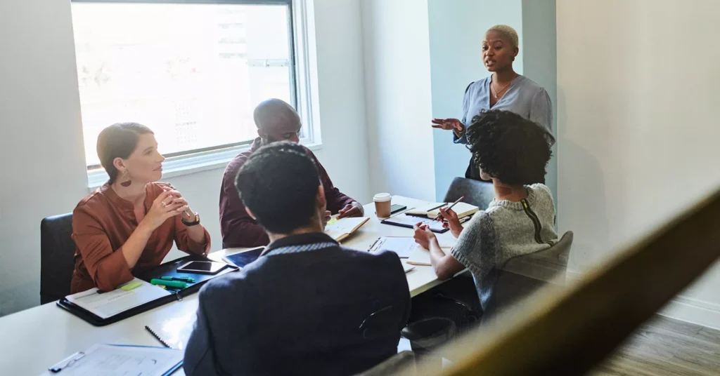 A team of safety leaders meet around a conference table with a woman leading the discussion about emergency response planning.