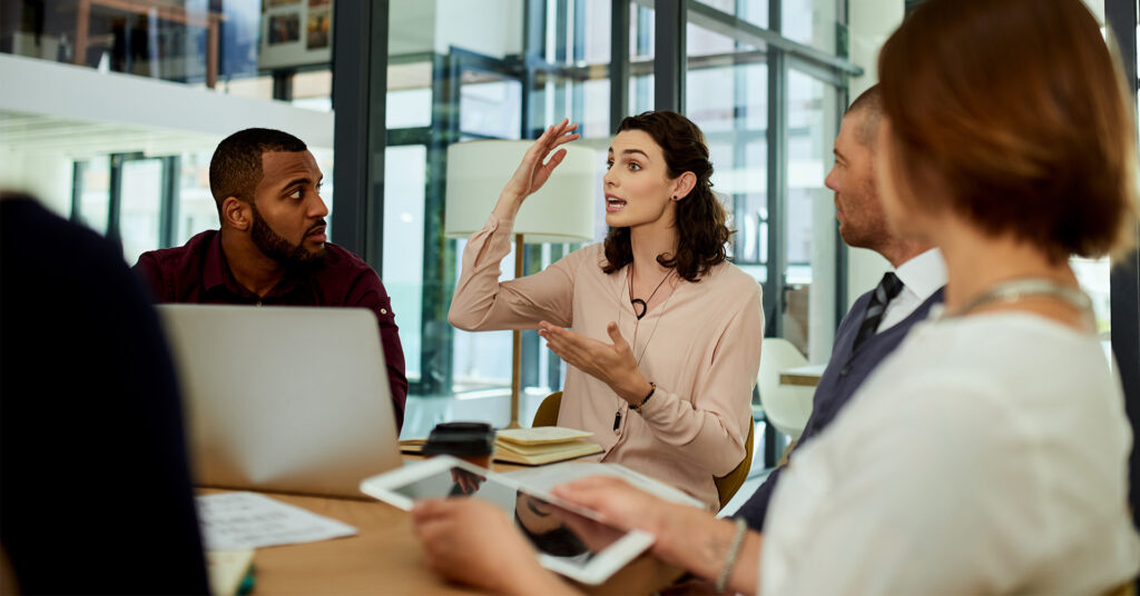 A group sits around a conference table discussing disaster recovery plans, and a woman gestures as she describes an incident