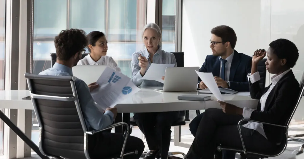 A group of coworkers sit around a conference table, holding papers, training in their company's business continuity plan