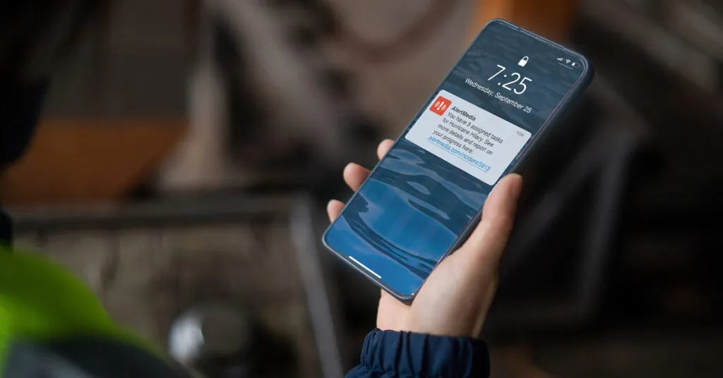 A hand holds a phone showing a mobile app notification with incident response tasks on the job.