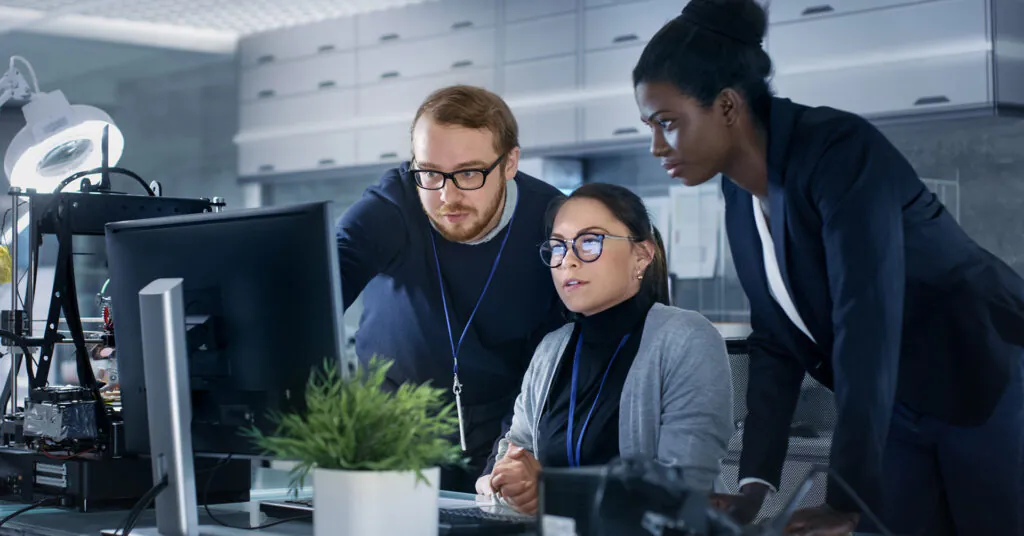 Three coworkers look intently at a computer monitor, one of them pointing at something on the screen