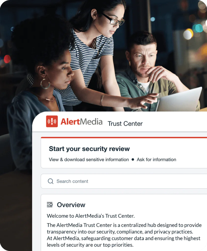 Three coworkers collaborate over a laptop behind an AlertMedia Trust Center screen showing security review tools, search, and privacy information.